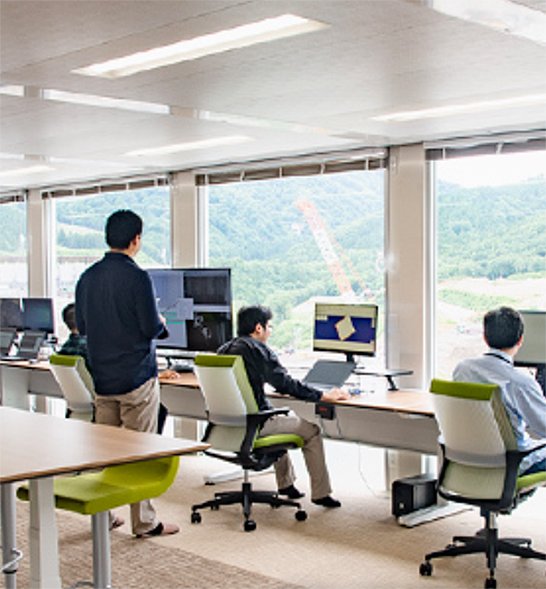 （図1）工事現場で管制室から自動化重機に指示を出すイメージ（出典：成瀬ダム堤体打設工事のWebサイトより引用）　イメージ